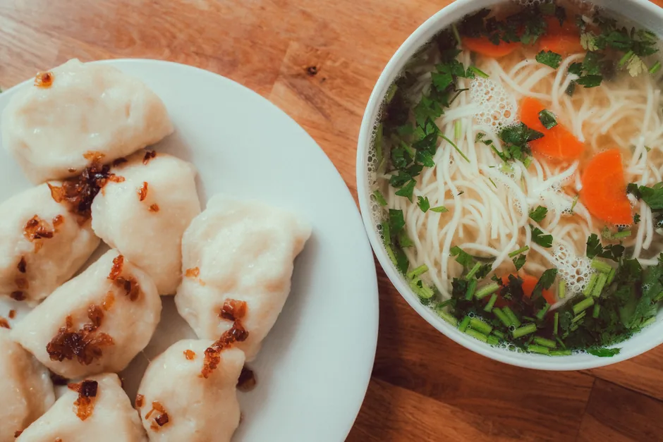 Pierogi dumplings beside a bowl of soup with noodles and vegetables